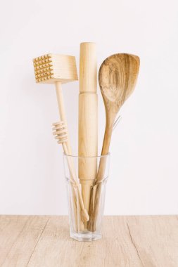 Beyaz arka planda bir bardakta ahşap mutfak eşyaları. Doğal malzemeler ve çevre dostu ev eşyaları.