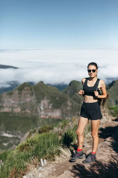 Fit girl in sports uniform on background of mountains and clouds. Trekking in the mountains, healthy lifestyle.
