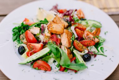 Terastaki ahşap masada ızgara somon dilimli taze sebze salatası..