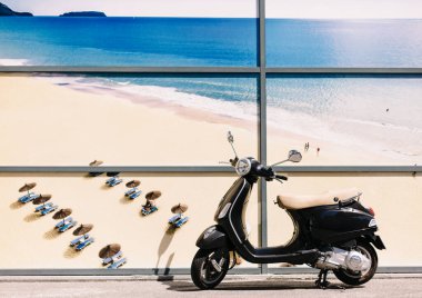 Scooter, kumlu bir plajın ve denizin arka planında. Büyük fotofon