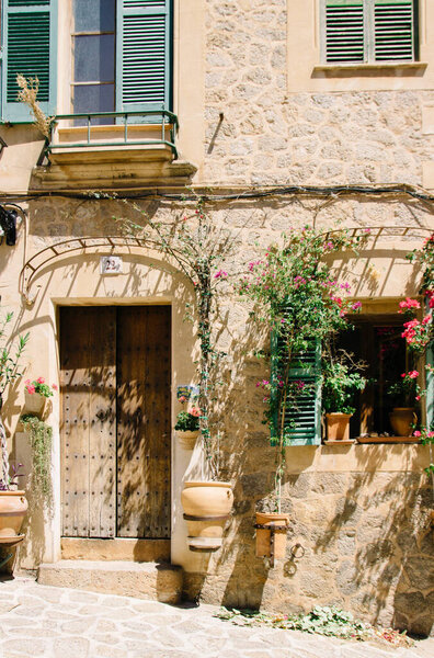 Mallorca, Spain - 30.06.2014. Entrance of an old house in Italy or Spain. Wooden doors, potted flowers, colored windows, sunlight. Travel and walking.