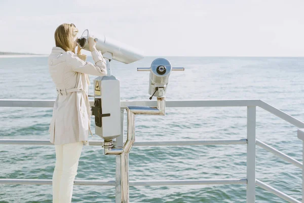 Woman explores the sea through stationary binoculars on the pier. Tourist on excursions