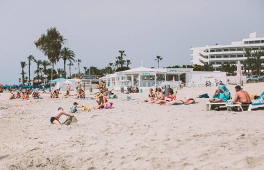 Ayia Napa, Kıbrıs - 01.05.2020. Yüksek turistik sezonda Nissi plajı. İnsanlar güneşlenir, çocuklar kaleler inşa eder..