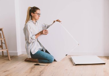 İş elbiseli güzel bir kadın parlak bir odada yerde oturuyor ve mobilyalarını açıyor.. 