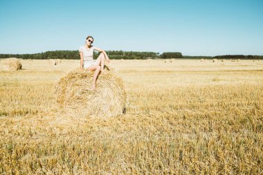 Buğday tarlaları. Yuvarlak saman topunun üzerinde oturan kız. Hasat, yazın sonu.. 