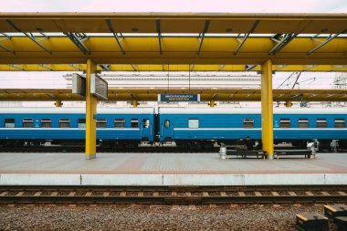 Minsk, Belarus - 01.08.2020. Tren İstasyonu. Mavi trenli platform, insanlar bankta oturuyor..