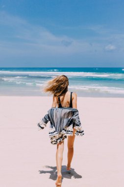 Terkedilmiş sahilde yürüyen güzel bir kız. Okyanus, mavi gökyüzü, beyaz kum.