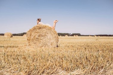 Samanlıkta takılan kız. Çiftlikte yaz. Sahada gökyüzüne karşı saman balyaları. Boşluğu kopyala.