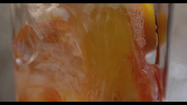 Nalijte oranžovou tekutinu do skleněného kelímku s ledem a pomerančem — Stock video