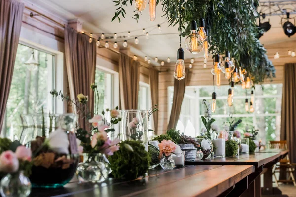 緑の花の枝で飾られたレースにかかってエジソン電球のガーランドとお祭りの結婚式のテーブル 粒状の効果 — ストック写真