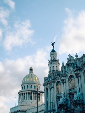 Havana 'nın iki ünlü simgesinin alçak açılı görüntüsü. El Capitolio 'nun altın kubbesi arka planda, Gran Teatro de la Habana' nın süslü, gri mimarisi ve heykel tepeli kulesiyle kısmen gizlenmiş..