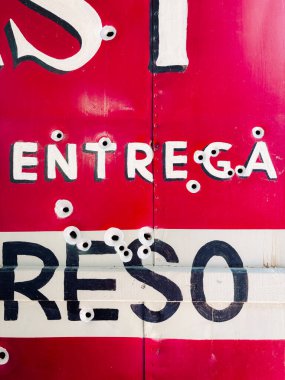 Siyah harfli kırmızı ve beyaz metal bir duvarın yakın plan, soyut bir fotoğrafı. Yüzeyde ezikler ve küçük kurşun delikleri var..