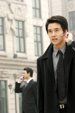 Diğer adam cep telefonuyla konuşurken bluetooth 'da konuşan bir adam.