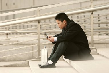 Takım elbiseli bir adam merdivenlerde oturmuş mesaj atıyor.