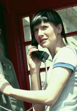 Telefon kulübesinde bekleyen bir bayan arama yapıyor.