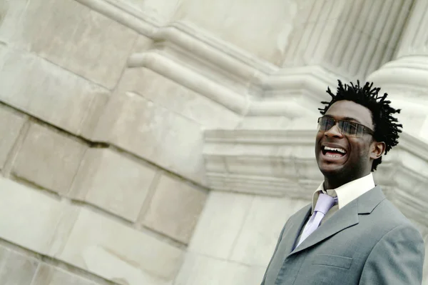 An African American man in business suit and sunglasses laughing while walking