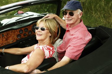 Çatısız arabalarında oturan, güneş gözlüklü evli bir çiftin arka planı.