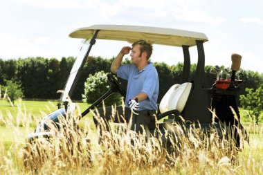 Golf arabasında oturan bir adam golf topunu arıyor.