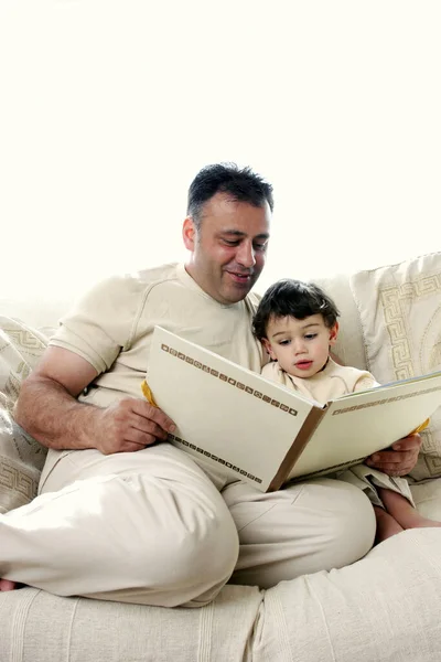 A man sitting on the couch reading a story book for his young son