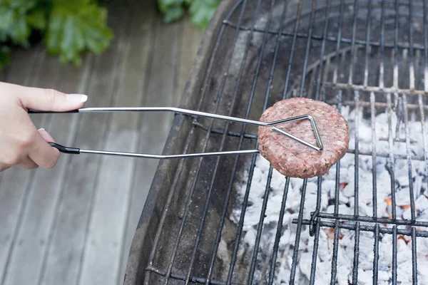 Human hand holding a beef patty with tongs