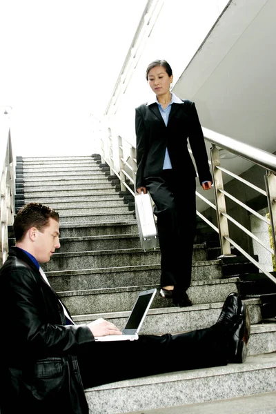 一个男人坐在楼梯上 用笔记本电脑 而一个女人走下楼梯 — 图库照片