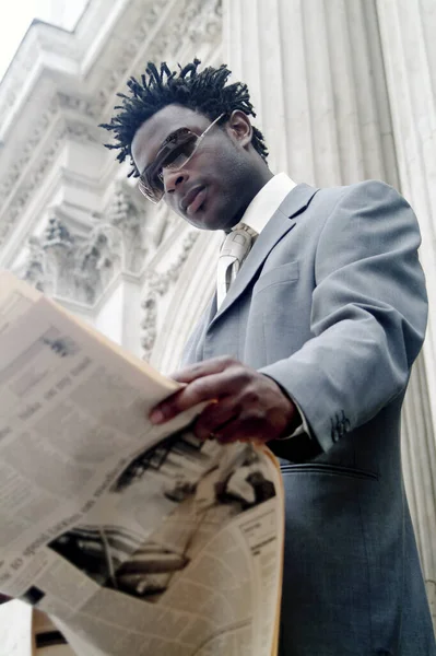 An African American man in business suit and sunglasses reading newspaper while standing