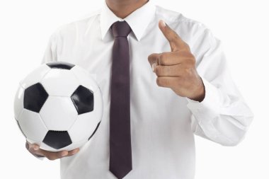 Futbol menajeri elinde bir top tutuyor ve işaret ediyor.