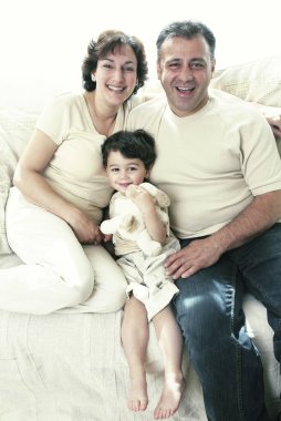 Küçük bir çocuk kanepede annesiyle babasının arasında oturuyor.