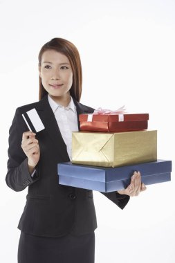 İş kadını bir yığın hediye kutusu taşıyor ve elinde bir kredi kartı tutuyor.