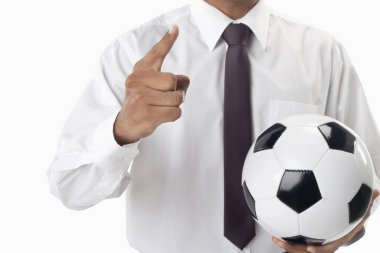 Futbol menajeri elinde bir top tutuyor ve işaret ediyor.
