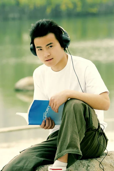 Göl Kenarında Oturmuş Kitap Okurken Kulaklıkla Müzik Dinleyen Bir Adam — Stok fotoğraf