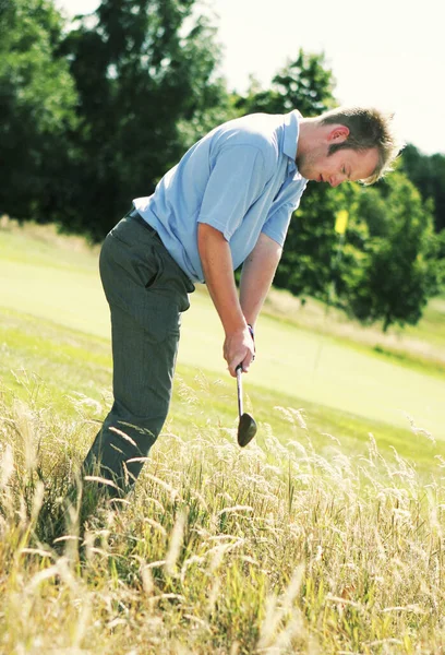 A guy aiming a golf ball trying to hit it