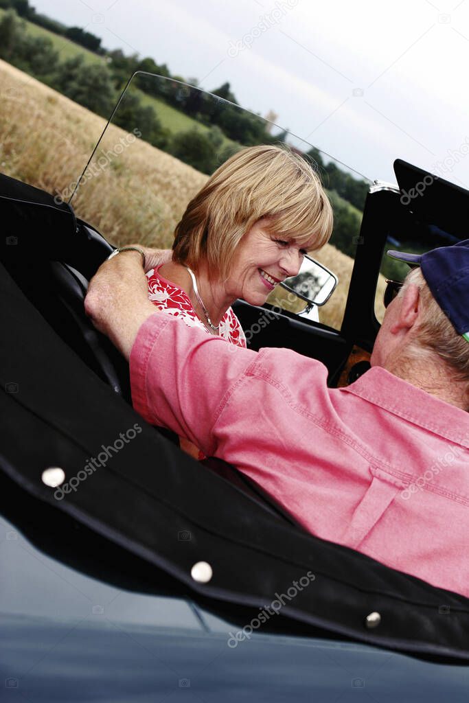 Back shot of an old man placing his hand around his wife's shoulder while sitting in the car