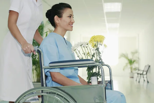 車椅子の女性を押す看護師 花の花瓶を持つ女性 — ストック写真
