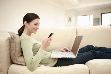 Kadın dizüstü bilgisayar kullanırken cep telefonundan mesaj atıyor