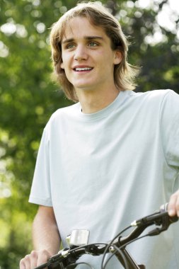 Genç adam parkta bisiklet sürüyor.