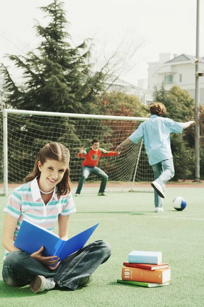 Девушка Читает Пока Друзья Играют Футбол — стоковое фото