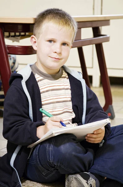 ペンと本を持ちながらカメラを見ている男の子 — ストック写真