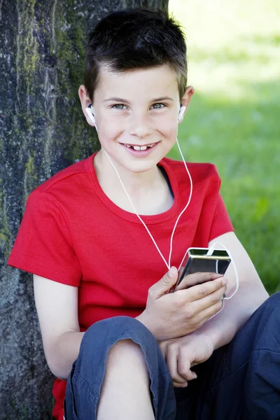 ポータブルMp3プレーヤーを聞いている間に木にもたれて男の子 — ストック写真