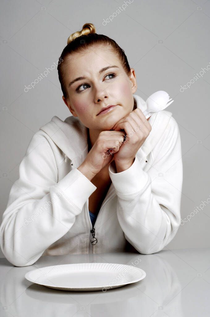 Woman sitting at table with empty plate and  thinking