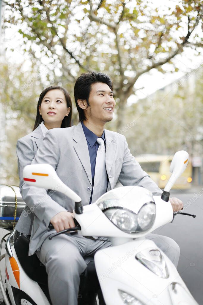Businessman and businesswoman riding on a scooter