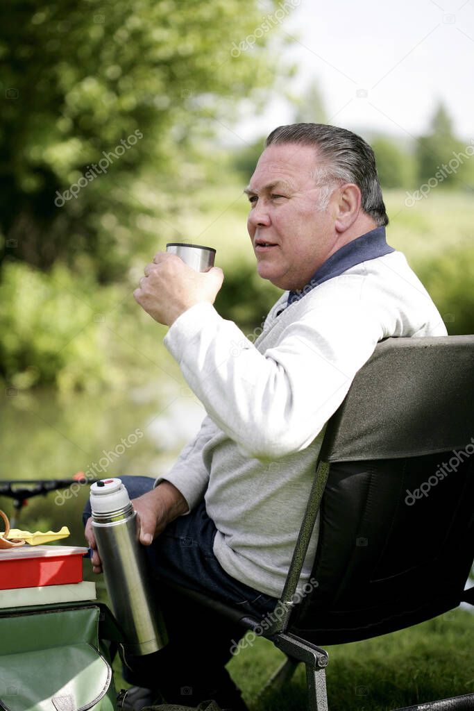 Senior man drinking while fishing by the river
