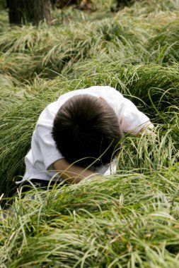 Genç çocuk çalıların altında arıyor.
