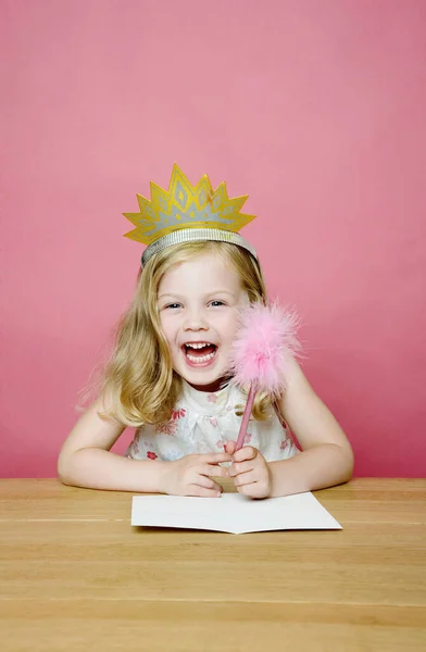 Girl with crown smiling while holding a pencil