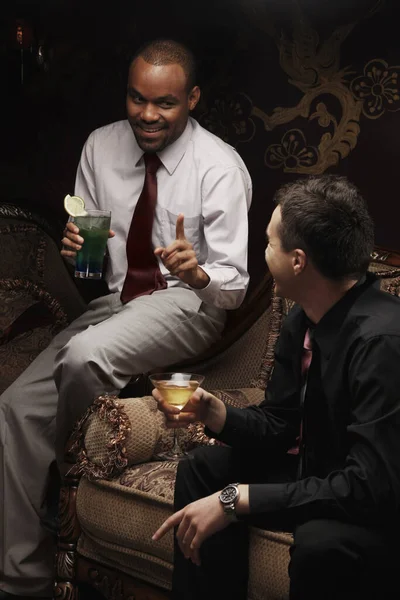 Businessmen sitting on antique sofa talking while having cocktails