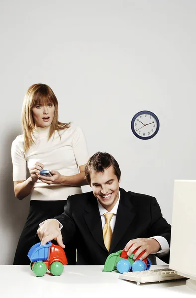 Businesswoman Using Palmtop While Her Colleague Playing Toy Cars — Stockfoto