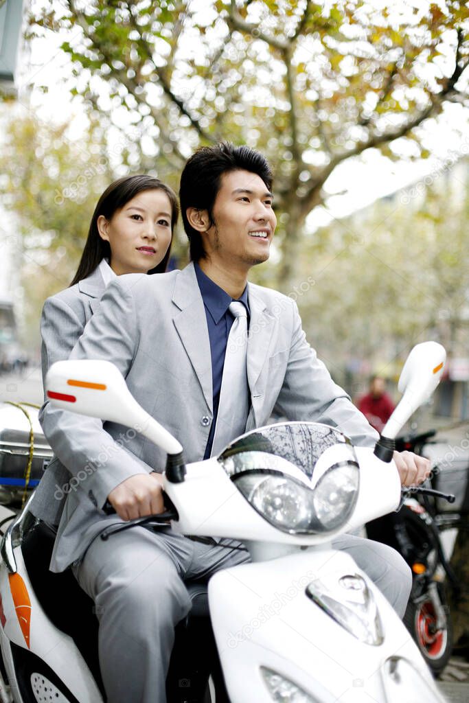 Businessman riding on a scooter with businesswoman sitting behind him