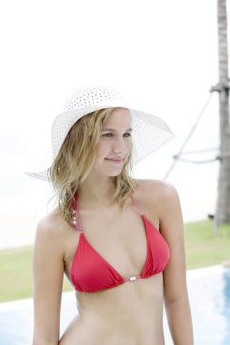 Bikinili ve şapkalı bir kadın başka tarafa bakarken gülümsüyor.