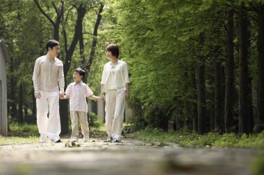 Çocuk parkta yürürken ebeveynleriyle el ele tutuşuyor.