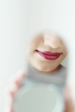 Pudra aynasında kırmızı ruj olan bir kadının dudaklarının yansıması.